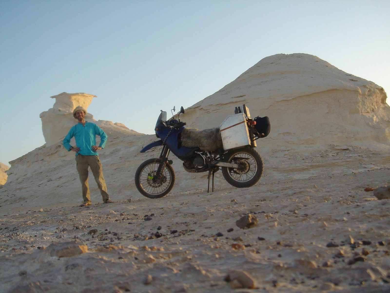 A man standing in dessert with motor bike