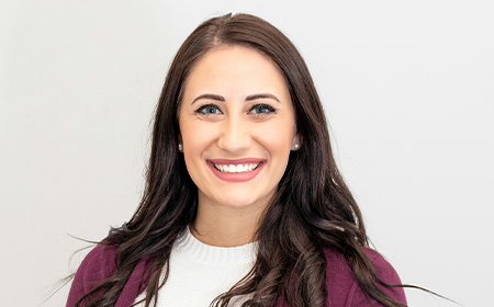 Woman with brown hair and a red jumper smiling to camera.
