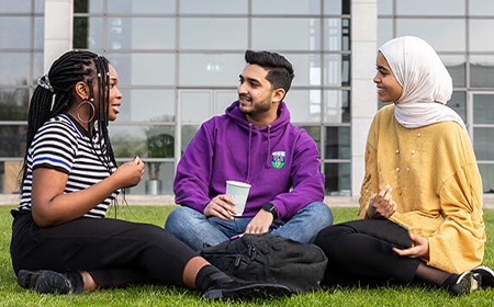 Three students sitting on the grass at UCD.