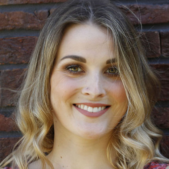 A headshot of a woman smiling into the camera with a brick wall in the background