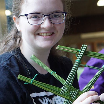 A student looking at camera smiling making St.Brigid's crosses