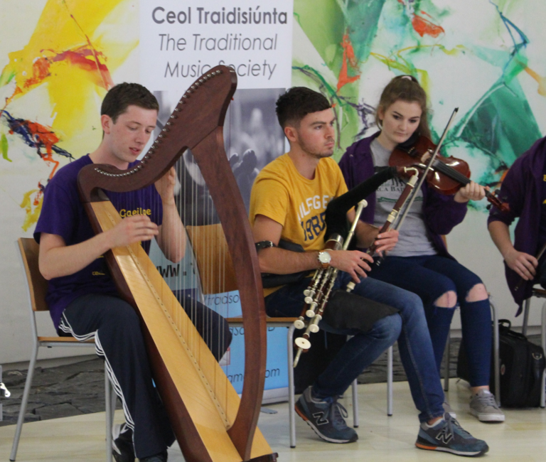 UCD students playing a large wooden harp, flute and fiddle