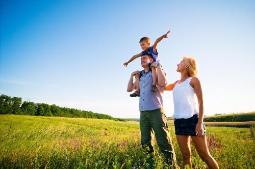 Family in field in sunshine, mother, father, son on fathers shoulders with arms out