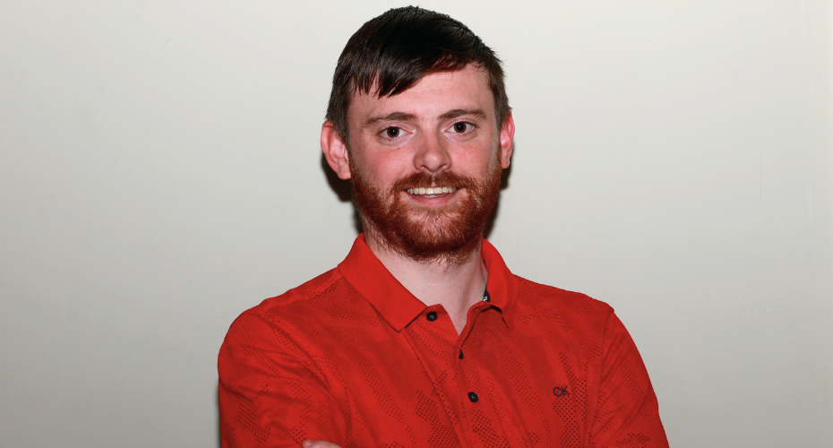 Dark haired man with a beard wearing a red top smiling to camera