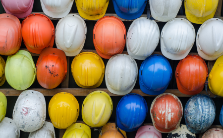 Hard hats of various colours hanging on a wooden fence