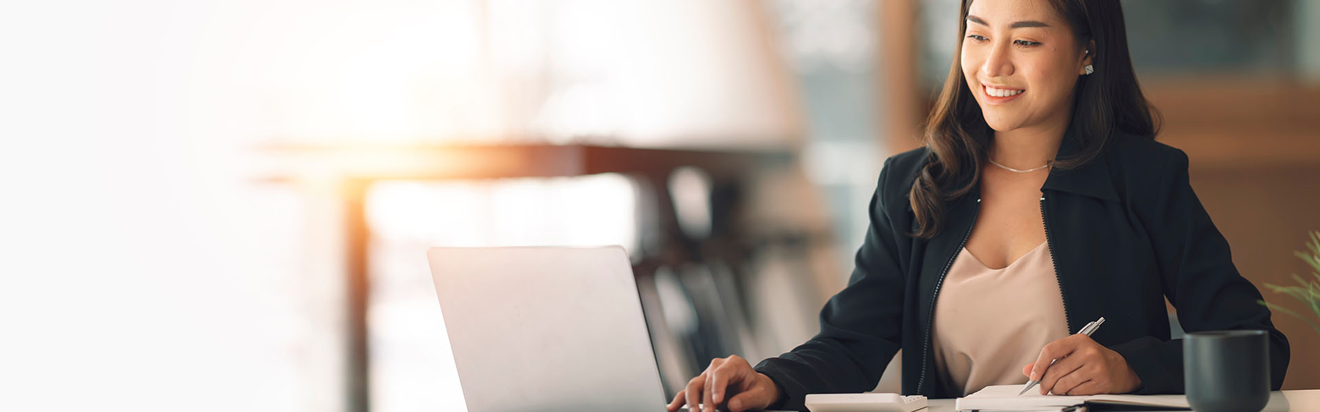 A woman working in front of a laptop and taking notes